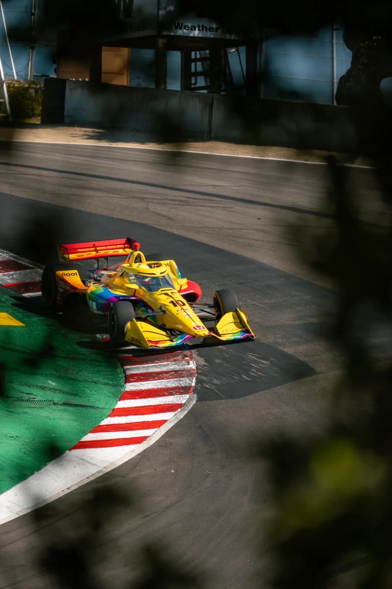 A vibrant racing car speeds around a corner on a track under bright sunlight.