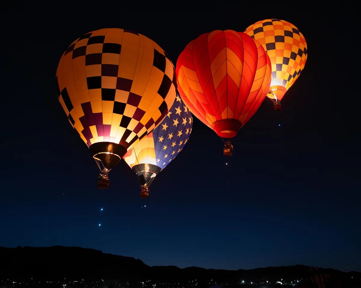 Three illuminated hot air balloons float against a dark sky during twilight hours.